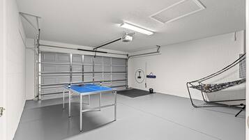 A spacious room with a ping pong table, a ceiling-mounted projector, and a wall-mounted exercise bike.