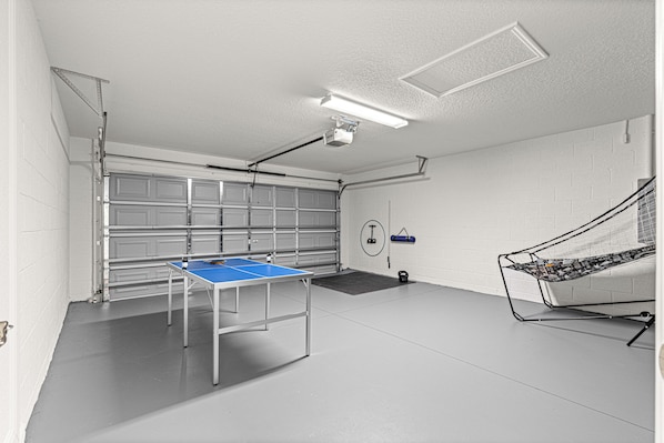 Una habitación amplia con mesa de ping pong, proyector instalado en el techo y bicicleta estática fijada a la pared.