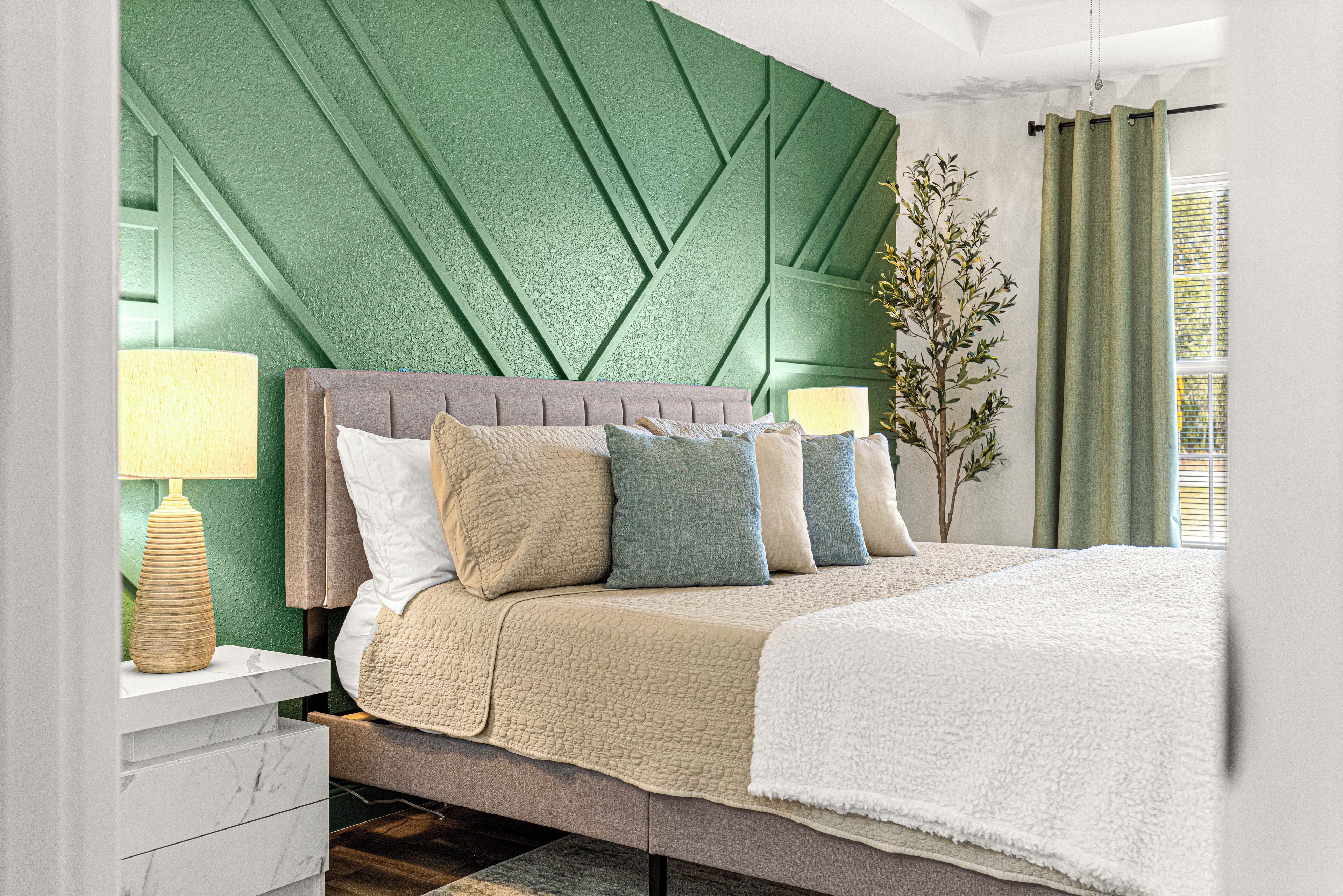 A modern bedroom with a green textured wall, a grey upholstered headboard, and a white bedspread.