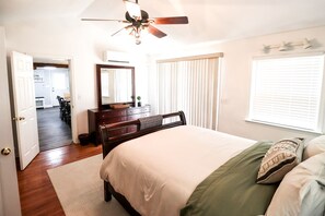 Une chambre à coucher comprenant un lit, une commode, un ventilateur de plafond et une fenêtre avec des stores.