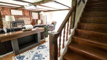 A cozy living room with a fireplace, a wooden staircase, and a stone wall.