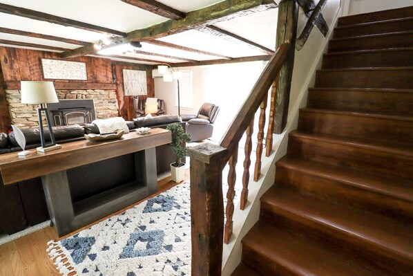 A cozy living room with a fireplace, a wooden staircase, and a stone wall.