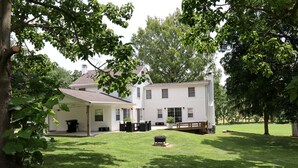 Een huis met twee verdiepingen, een overdekt terras, een barbecue en een verzorgd gazon.