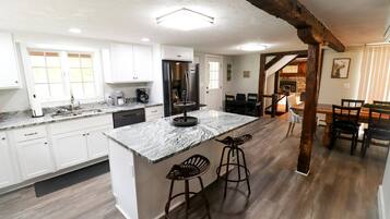 A kitchen with white cabinets, a marble island, and a dining area with wooden chairs and a table.