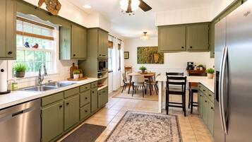 Una cocina con gabinetes verdes, un refrigerador de acero inoxidable, un ventilador de techo y una zona de comedor con sillas y una mesa.