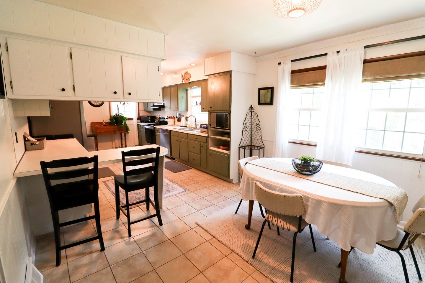 A compact kitchen with white cabinets, a dining table with chairs, and a window with curtains.