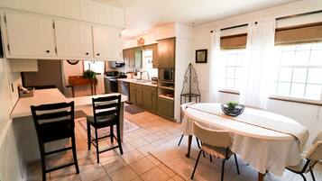 A compact kitchen with white cabinets, a dining table with chairs, and a window with curtains.