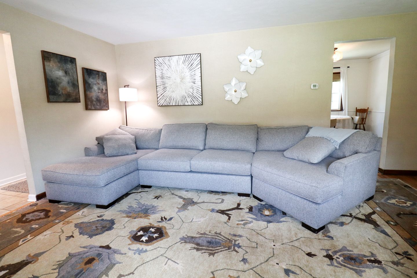 A living room with a sectional sofa, a patterned rug, and wall art.