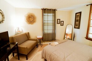 A hotel room with a bed, a sofa, a small table, a TV, and a window with curtains.
