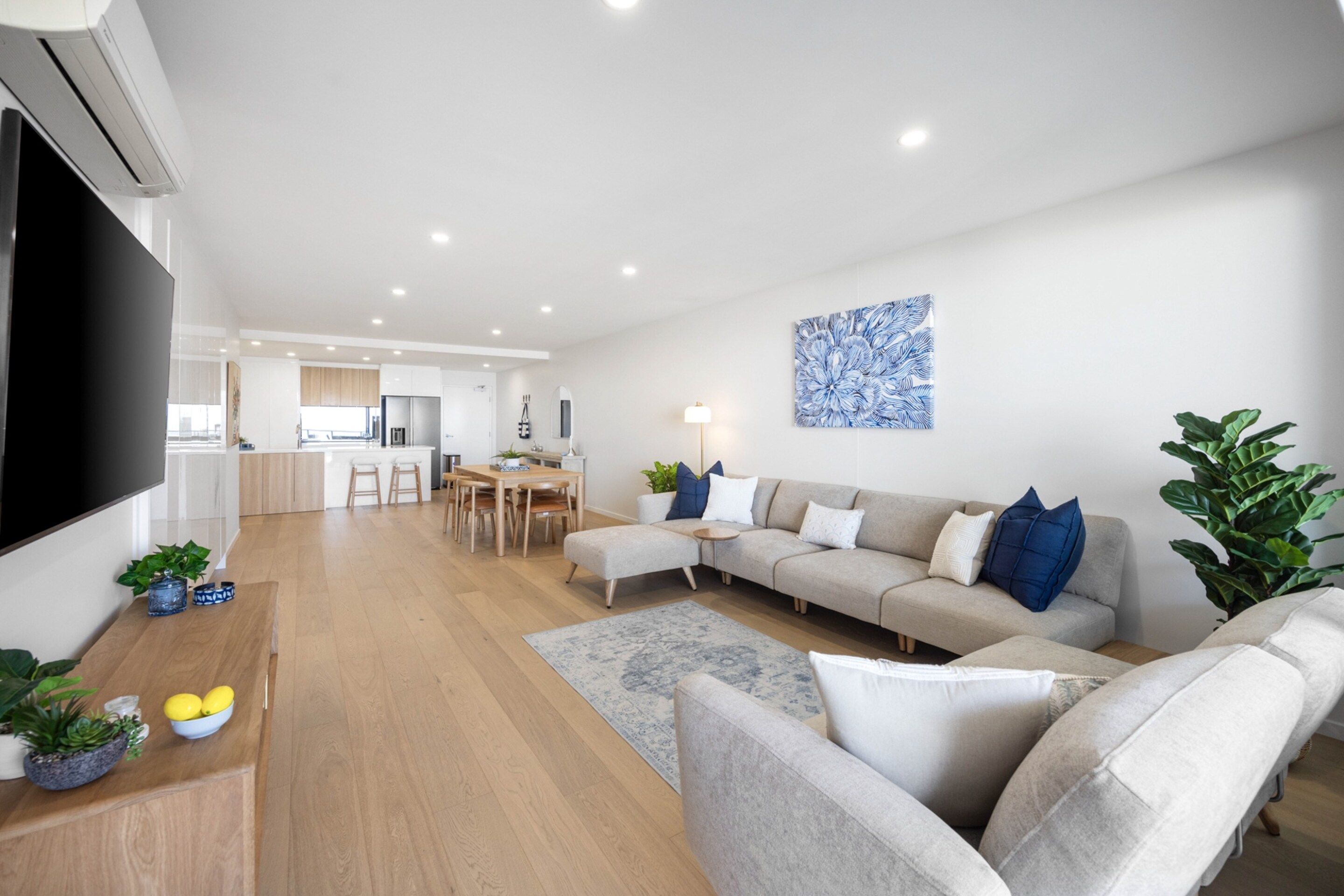 A modern living room with a grey sofa, a flat-screen TV, and a dining area with a wooden table and chairs.