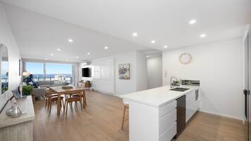 A modern kitchen with a central island, a dining area with a sofa and chairs, and a view of the sea through large windows.