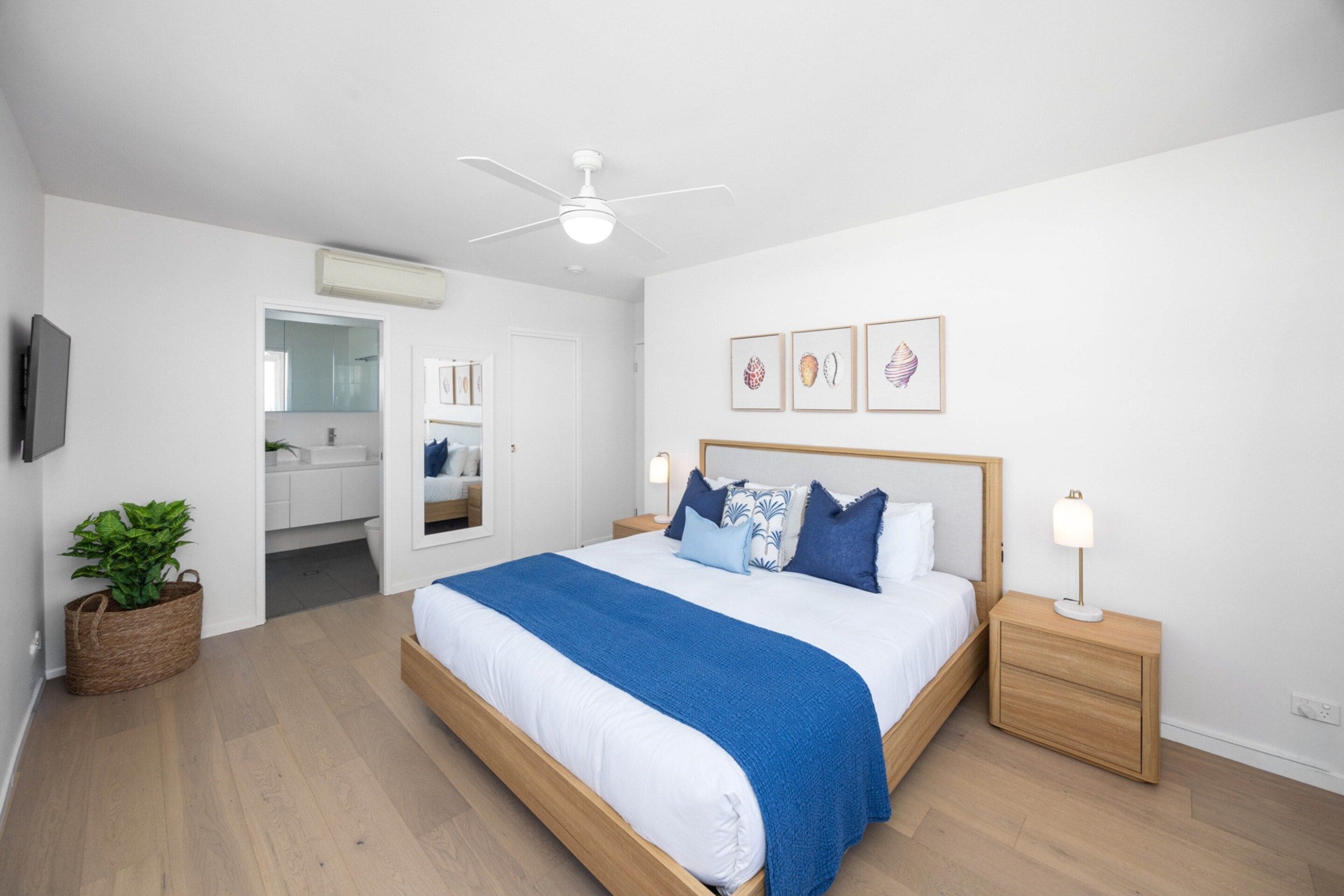 A bedroom with a bed, bedside tables, a ceiling fan, a wall-mounted TV, and framed artwork.