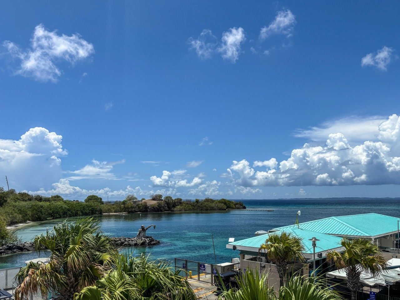 A coastal view with a clear sky, a swimming pool, and lush greenery.