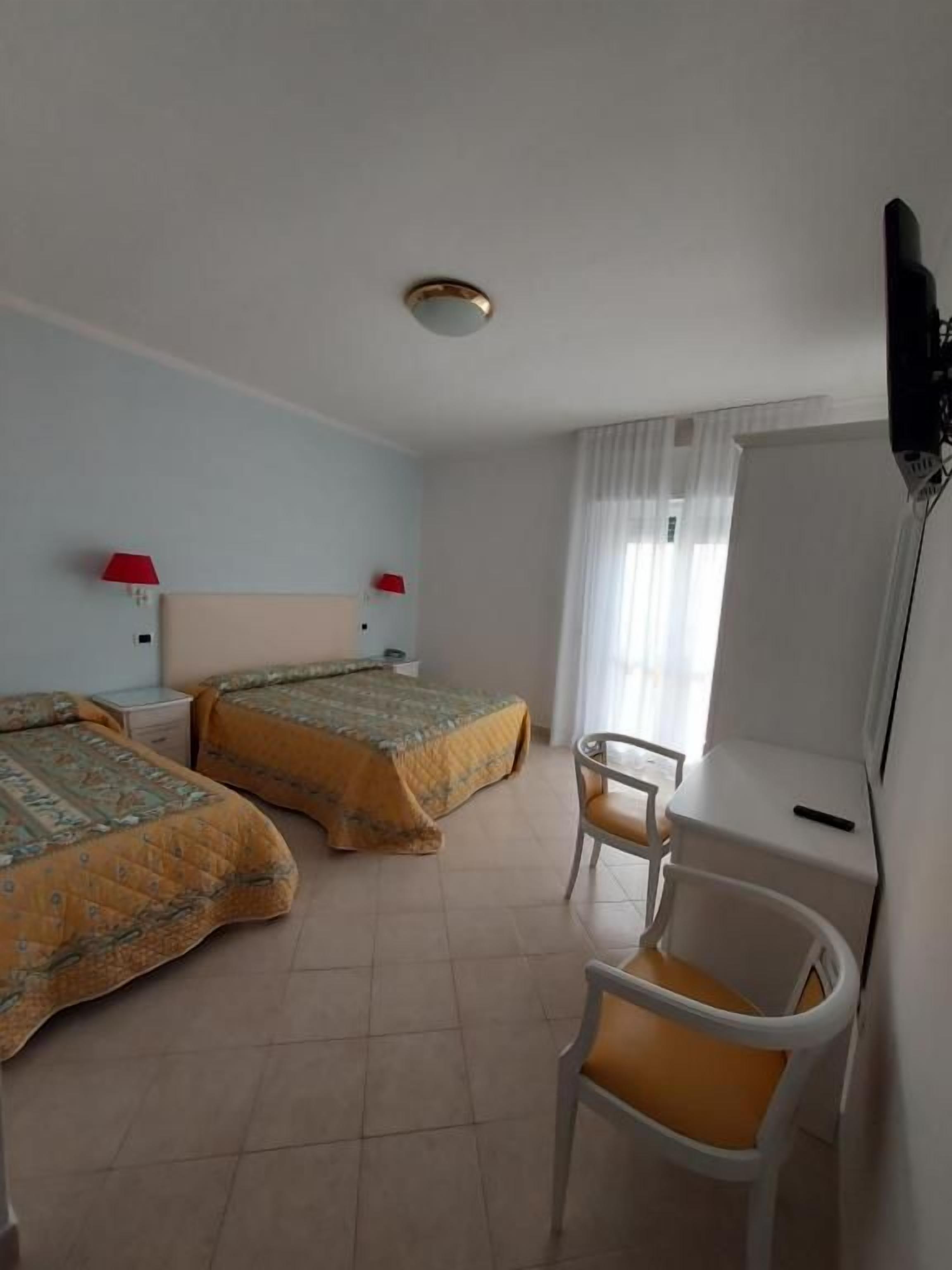 A hotel room with two beds, a desk, a chair, a television, and a window with curtains.