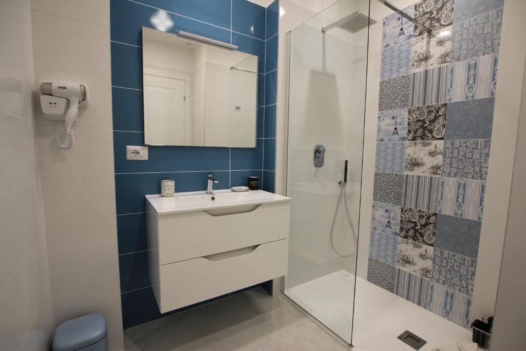Een moderne badkamer met een glazen douchecabine, een witte wastafel met spiegel en een wand betegeld met blauwe tegels.