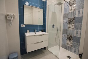 Casa de banho moderna com cabine de duche em vidro, toucador branco com espelho e parede revestida a azulejos azuis.