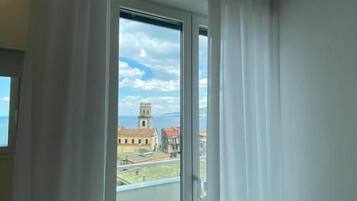 A room with a large window, curtains, and a view of a building with a tower.