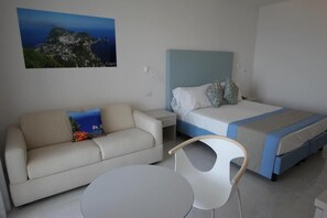 Quarto de hotel com cama, sofá, cadeira e mesa pequena.