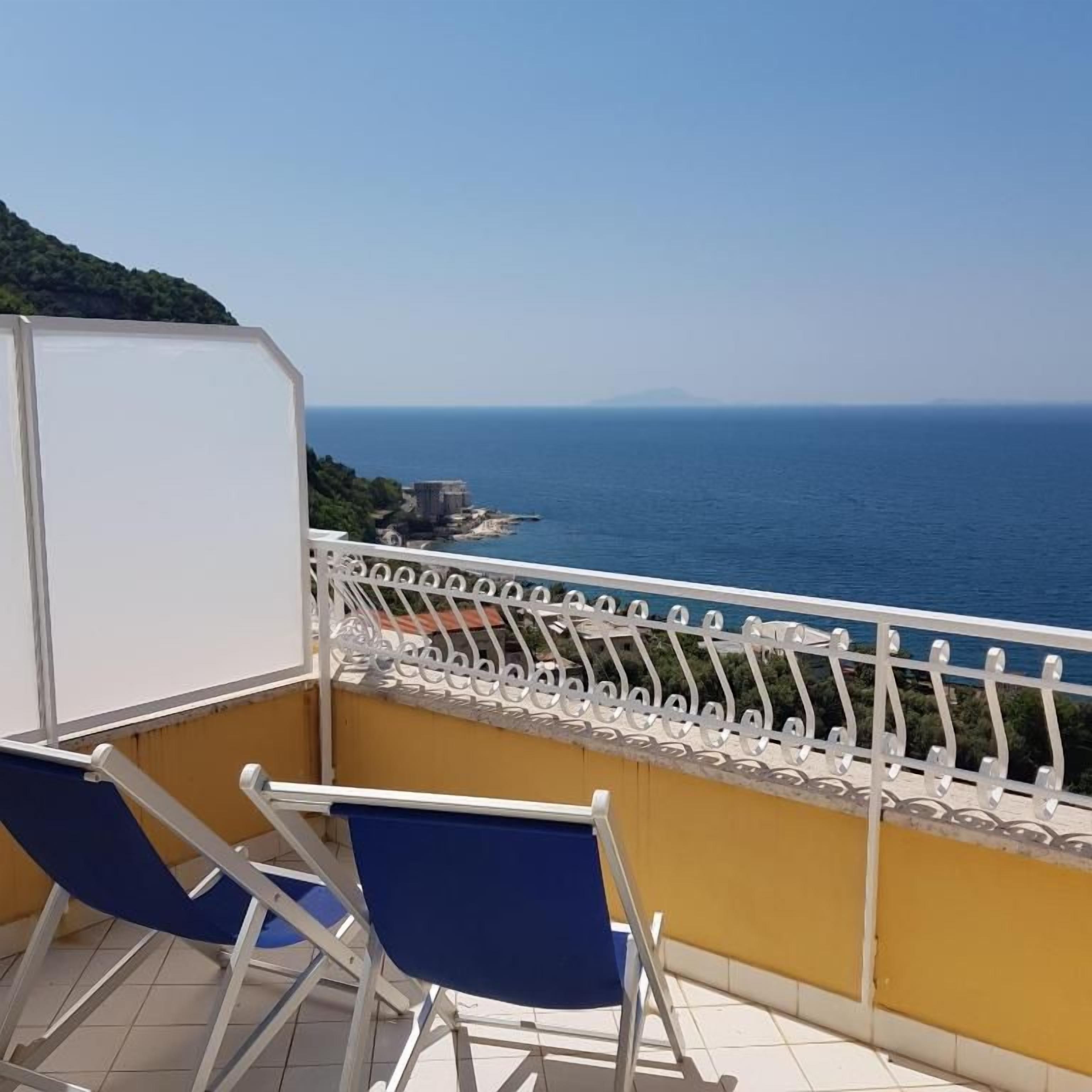 Ein Balkon mit Meerblick, zwei blaue Stühle und ein weißes Geländer.