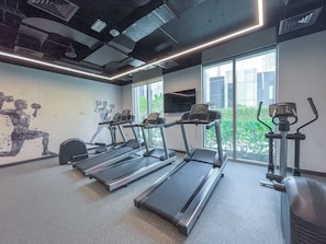 A gym with treadmills, exercise bikes, and a large window with a view of buildings and greenery. - StayShort - Stylish 4-Bedroom Oasis  in Peaceful Creek Harbour! (Dubai Creek Harbour)