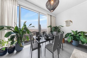 A modern dining room with a city view, large windows, and potted plants. - StayShort - Stylish 4-Bedroom Oasis  in Peaceful Creek Harbour! (Dubai Creek Harbour)