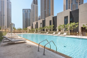 A swimming pool with lounge chairs and a view of tall buildings. - StayShort - Stylish 4-Bedroom Oasis  in Peaceful Creek Harbour! (Dubai Creek Harbour)