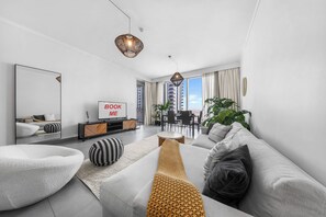 Ein modernes Wohnzimmer mit einer Couch, einem Couchtisch, einem Fernseher und einem Essbereich mit Stühlen und Tisch.