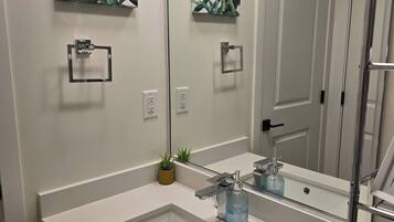 Un baño con un espejo grande, un lavabo, un perchero para toallas y una planta en maceta.