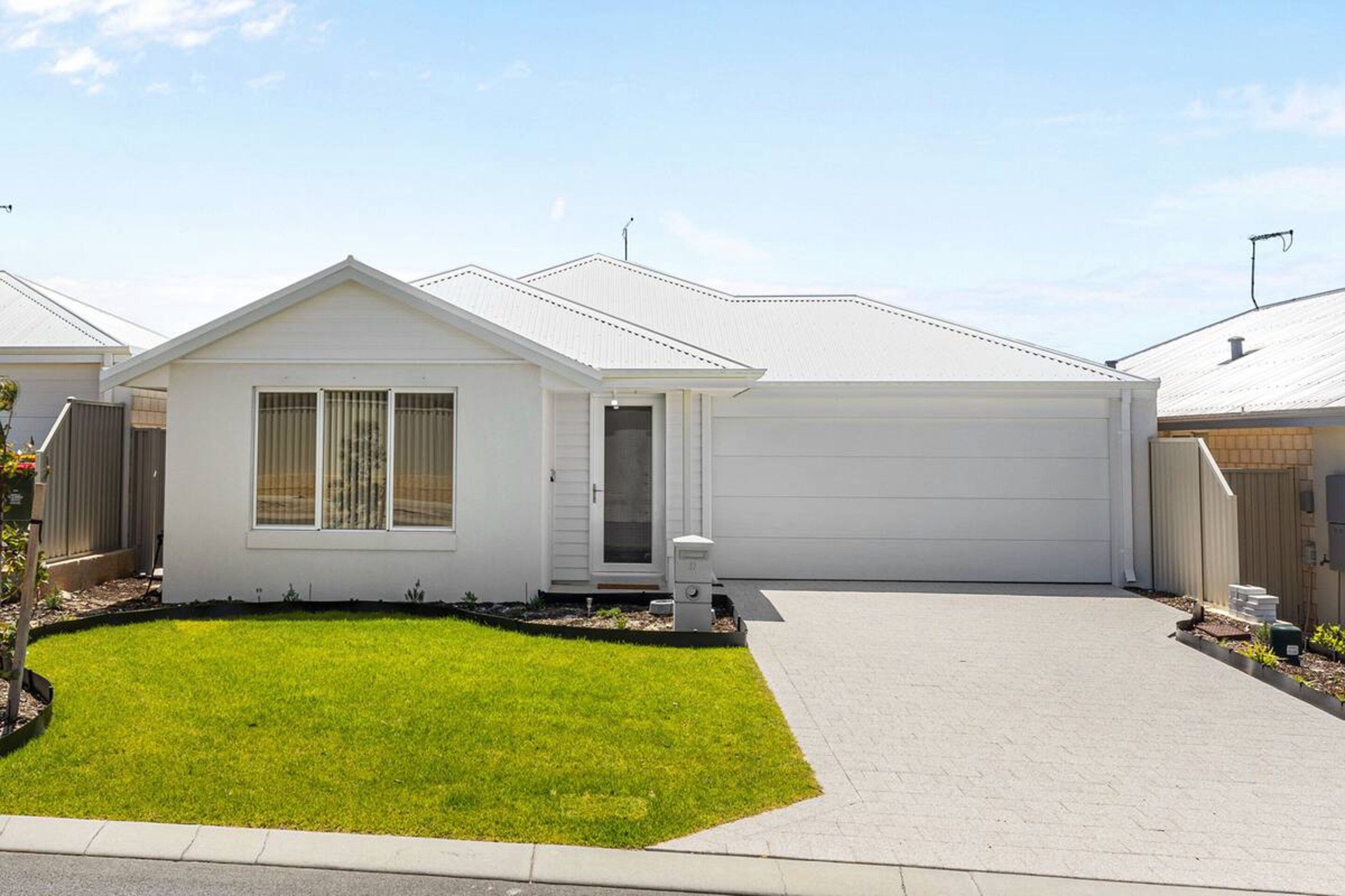 A single-story residential house with a front garage, a well-maintained lawn, and a clear sky.