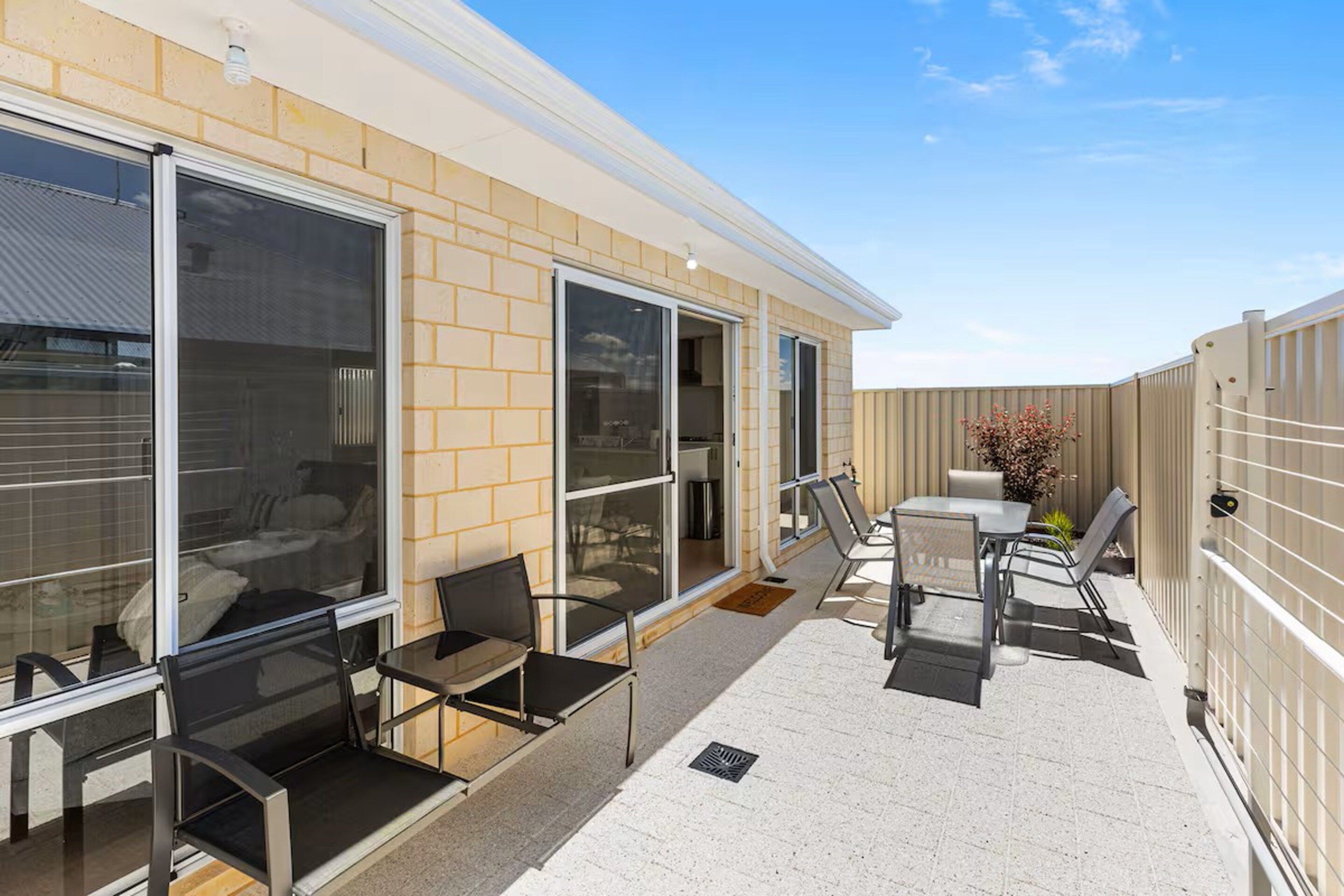A covered outdoor patio with a seating area, including a table and chairs, and a sliding glass door leading to an interior space.