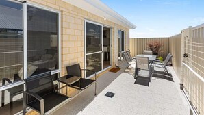 A covered outdoor patio with a seating area, including a table and chairs, and a sliding glass door leading to an interior space. - Alkimos Coastal Escape (Alkimos)