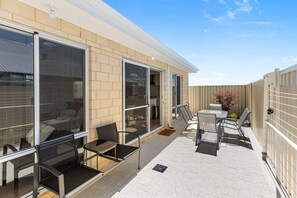 A covered outdoor patio with a seating area, including a table and chairs, and a sliding glass door leading to an interior space. - Alkimos Coastal Escape (Alkimos)
