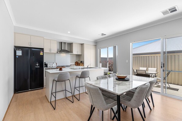 A modern kitchen with a black refrigerator, white cabinets, and a central island with bar stools. - Alkimos Coastal Escape (Alkimos)