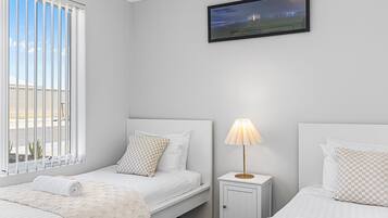 A hotel room with two beds, a television mounted on the wall, and a window with blinds.