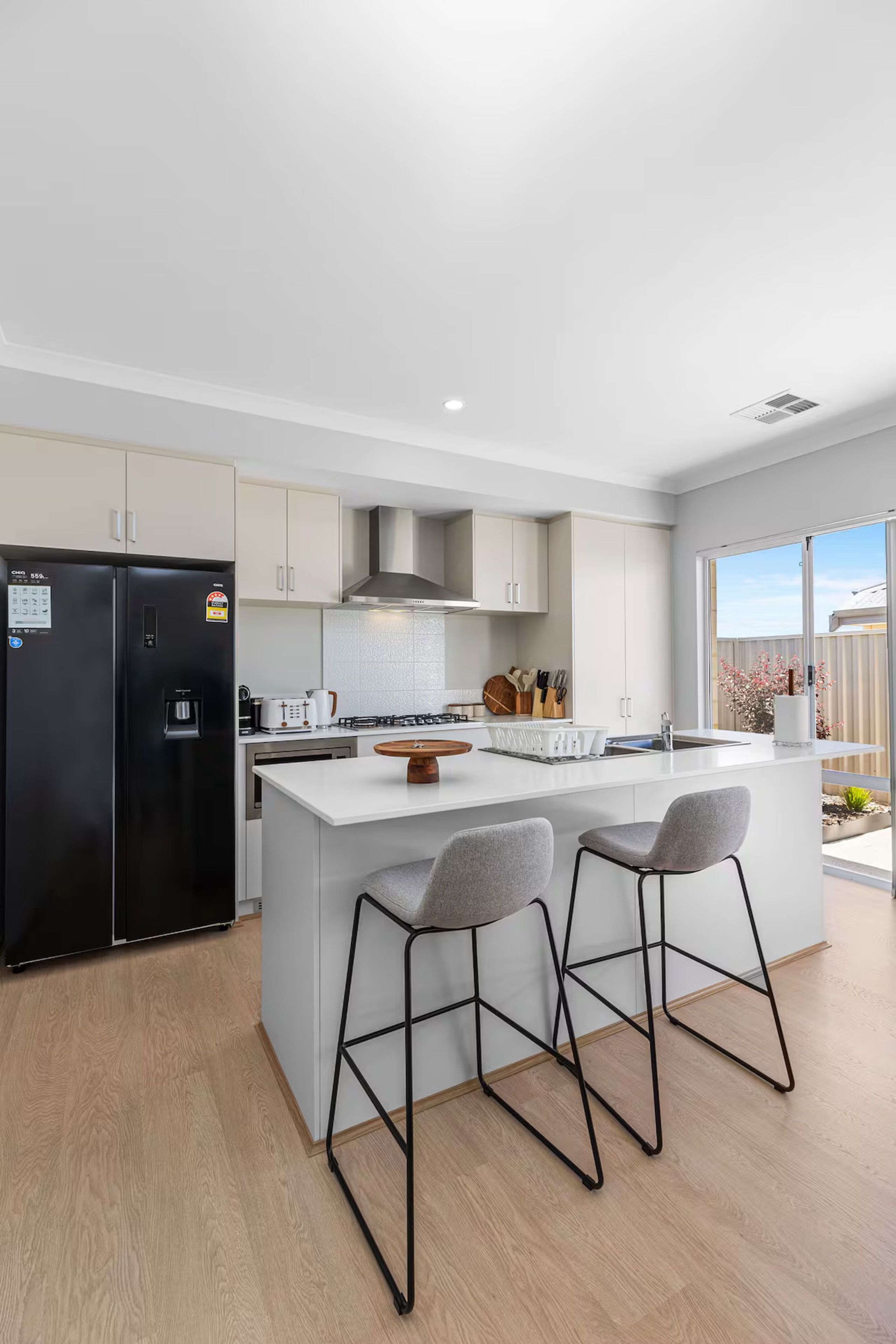 A modern kitchen with a central island, bar stools, a black refrigerator, and a gas stove.