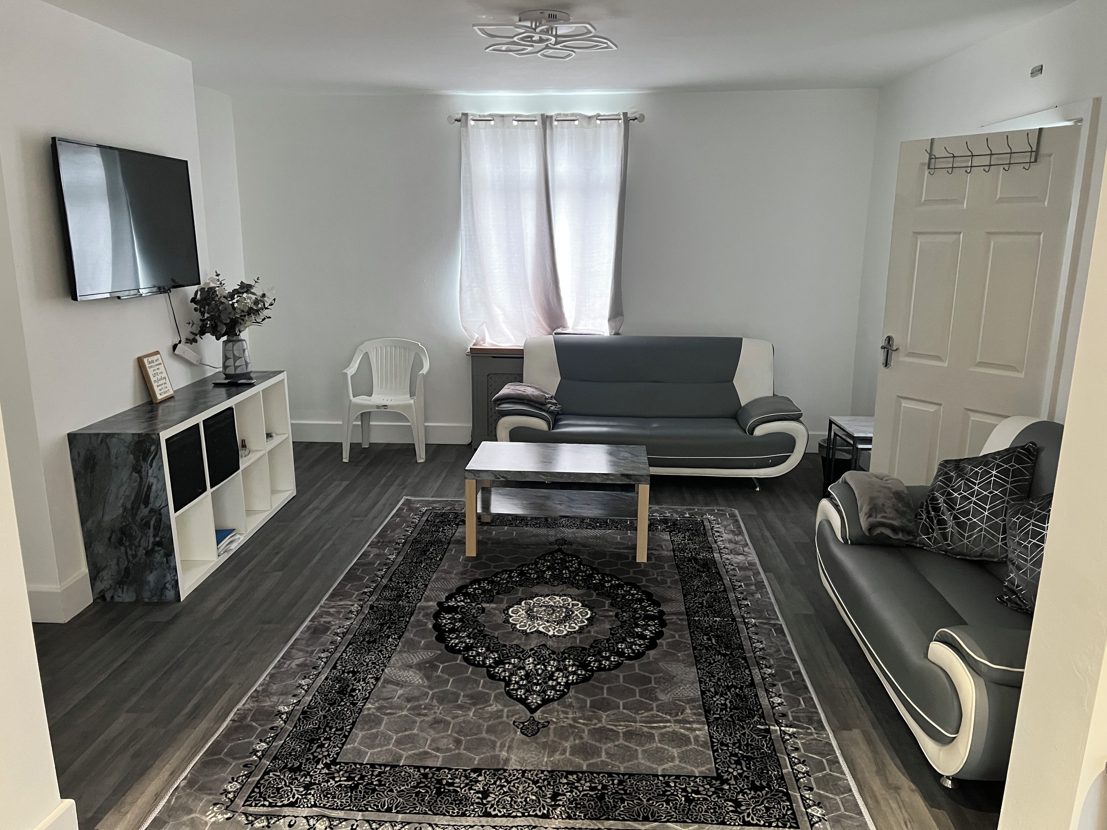 A modern living room with a grey sofa, a coffee table, a TV mounted on the wall, and a patterned rug.