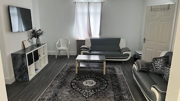 A modern living room with a grey sofa, a coffee table, a TV mounted on the wall, and a patterned rug.