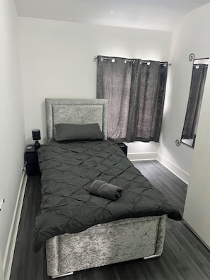Una cama bien hecha con cabecera, una mesita de noche con lámpara y una ventana con cortinas.