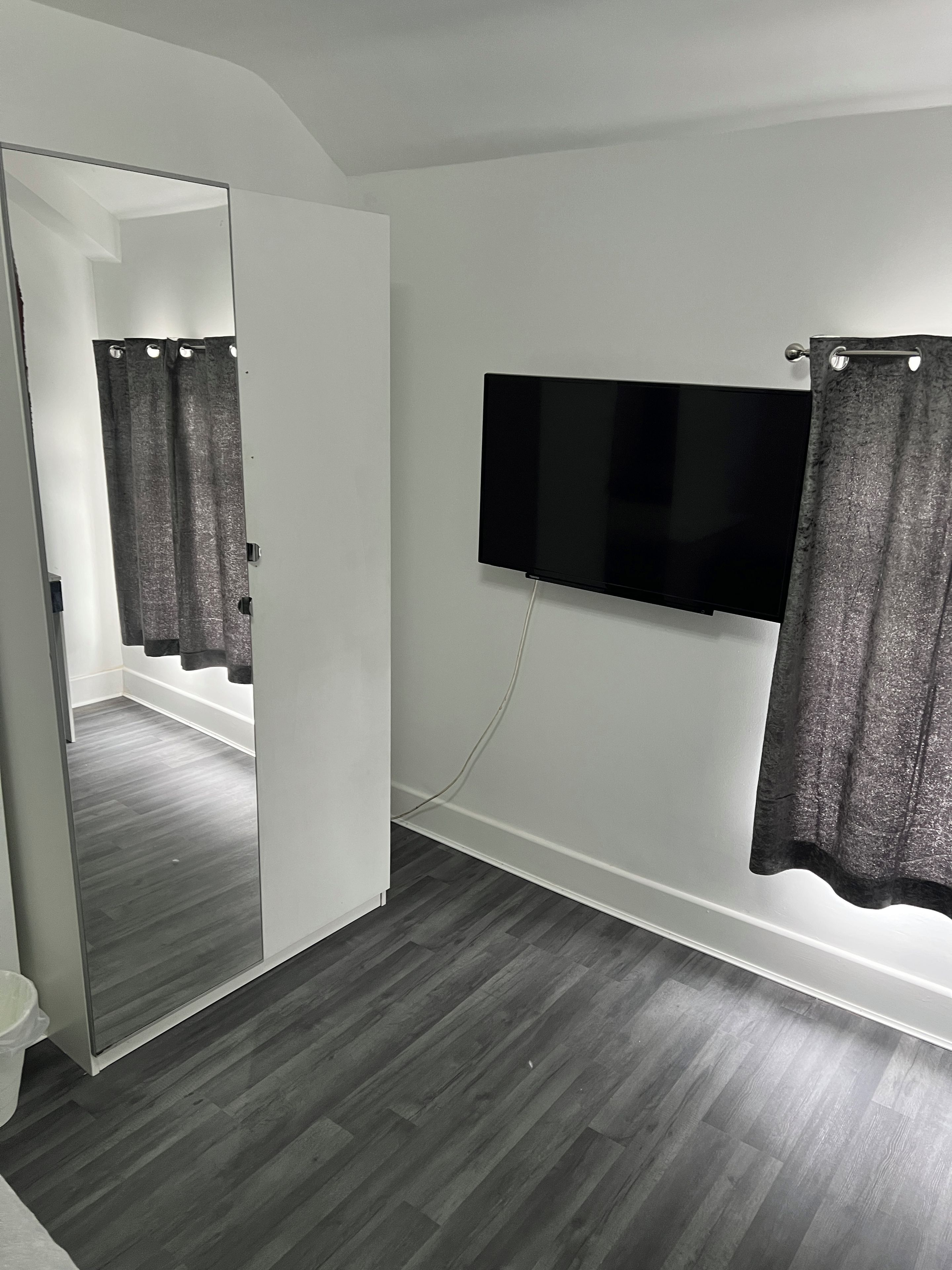 A room with a large mirror, a flat-screen TV mounted on the wall, and a shower area with curtains.