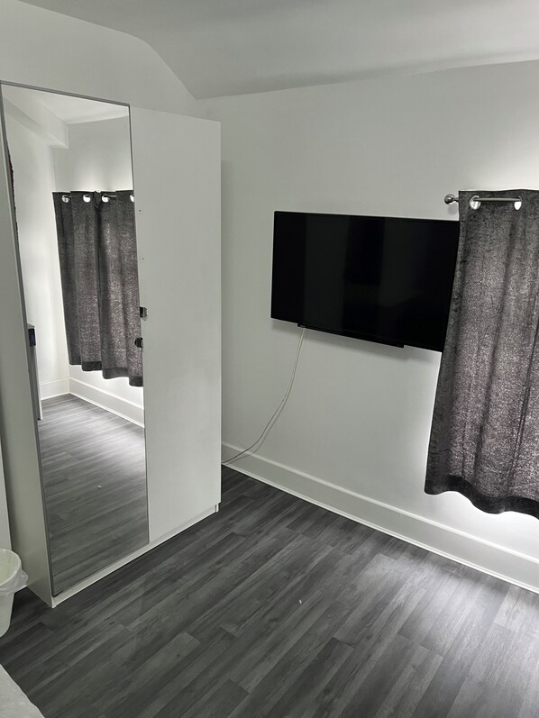 A room with a large mirror, a flat-screen TV mounted on the wall, and a shower area with curtains.