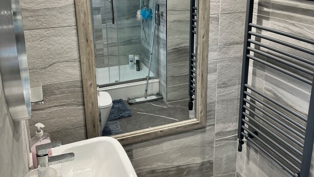 Moderni kylpyhuone, jossa on lasiseinällä varustettu suihku, valkoinen pesuallas ja pyyhekoukku.