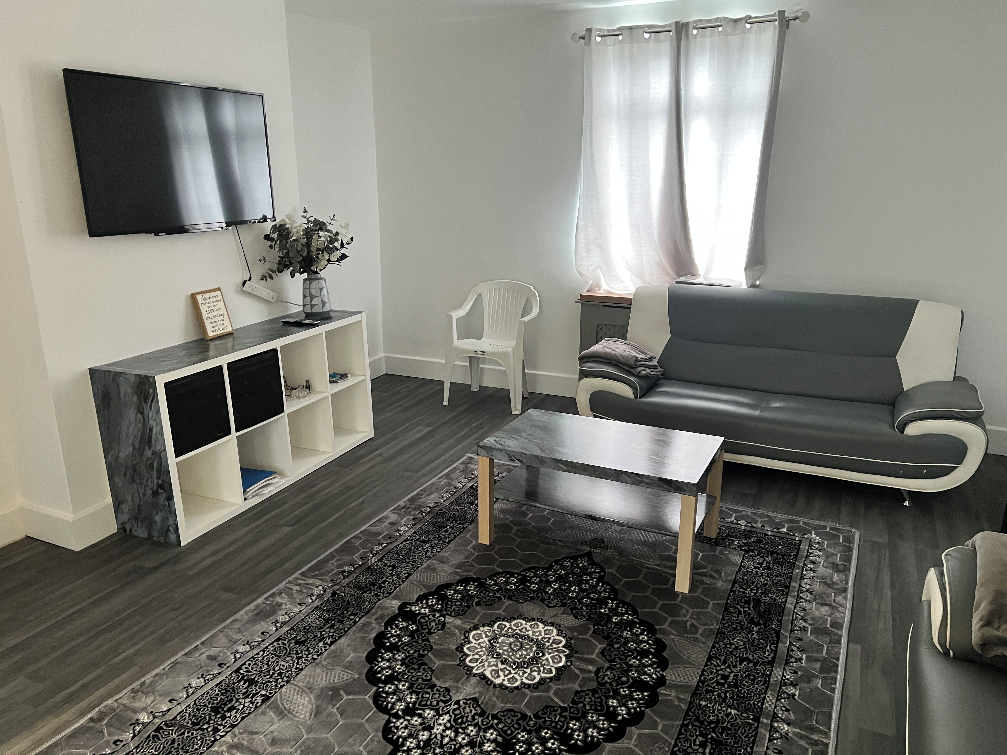 A modern living room with a flat-screen TV, a sofa, a coffee table, and a patterned rug.