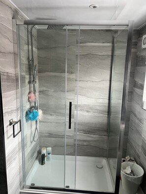 Un box de ducha moderno con puerta de cristal, cabezal de ducha manual y cabezal de ducha manual con un accesorio en forma de rosetón.