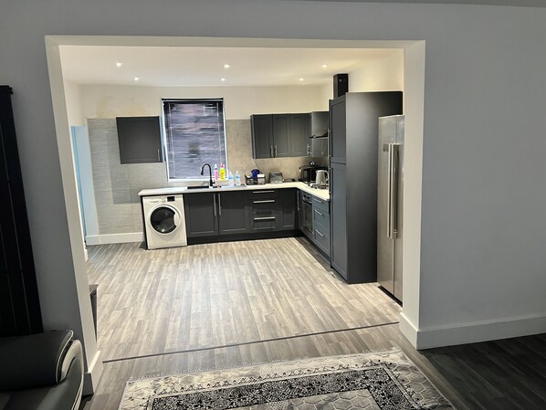 A modern kitchen with grey cabinets, a built-in washing machine, and a stainless steel refrigerator.