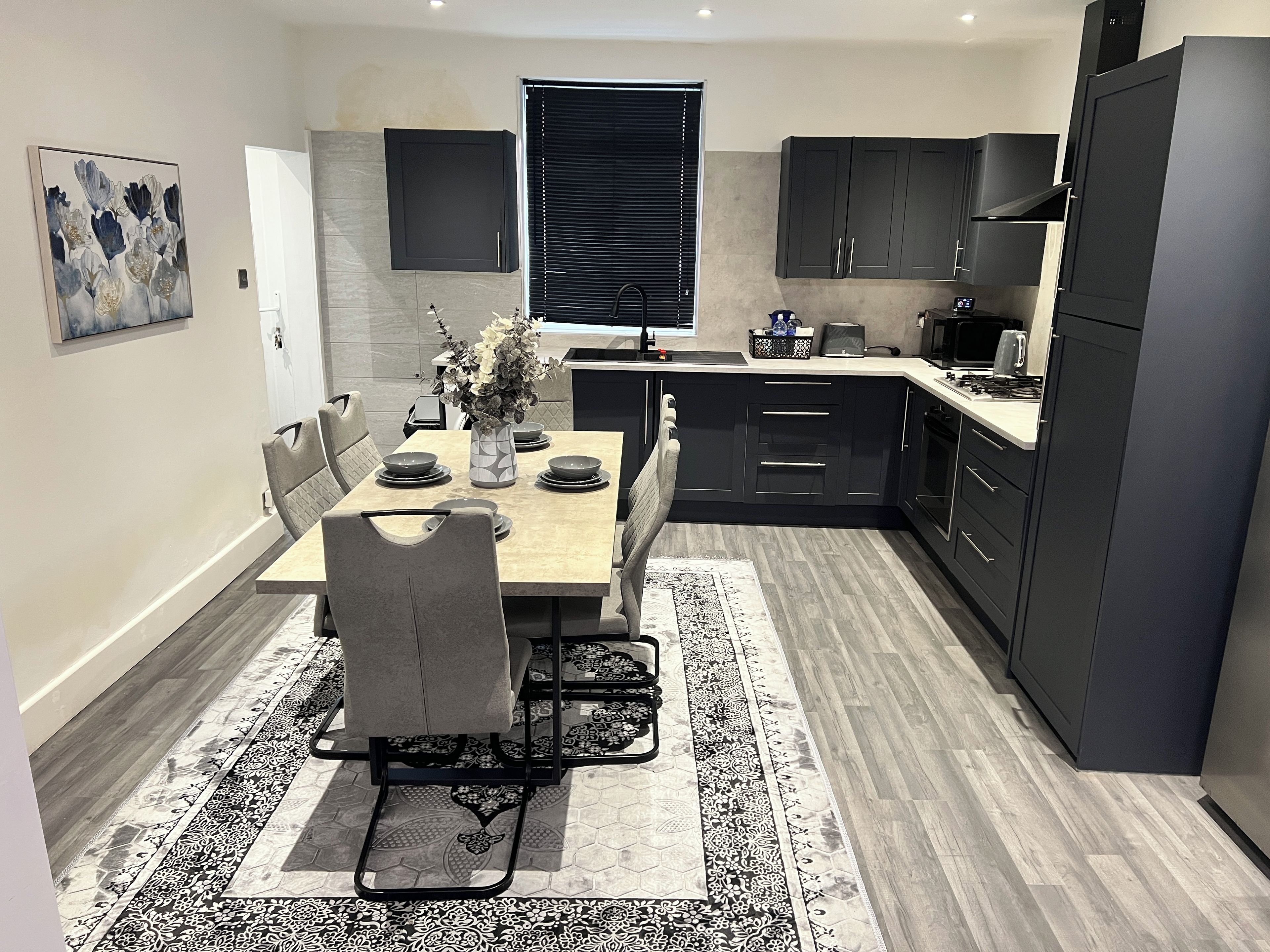 A modern kitchen with dark cabinetry, a dining table with chairs, and a black and white patterned rug.