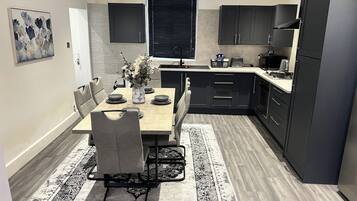 A modern kitchen with dark cabinetry, a dining table with chairs, and a black and white patterned rug.