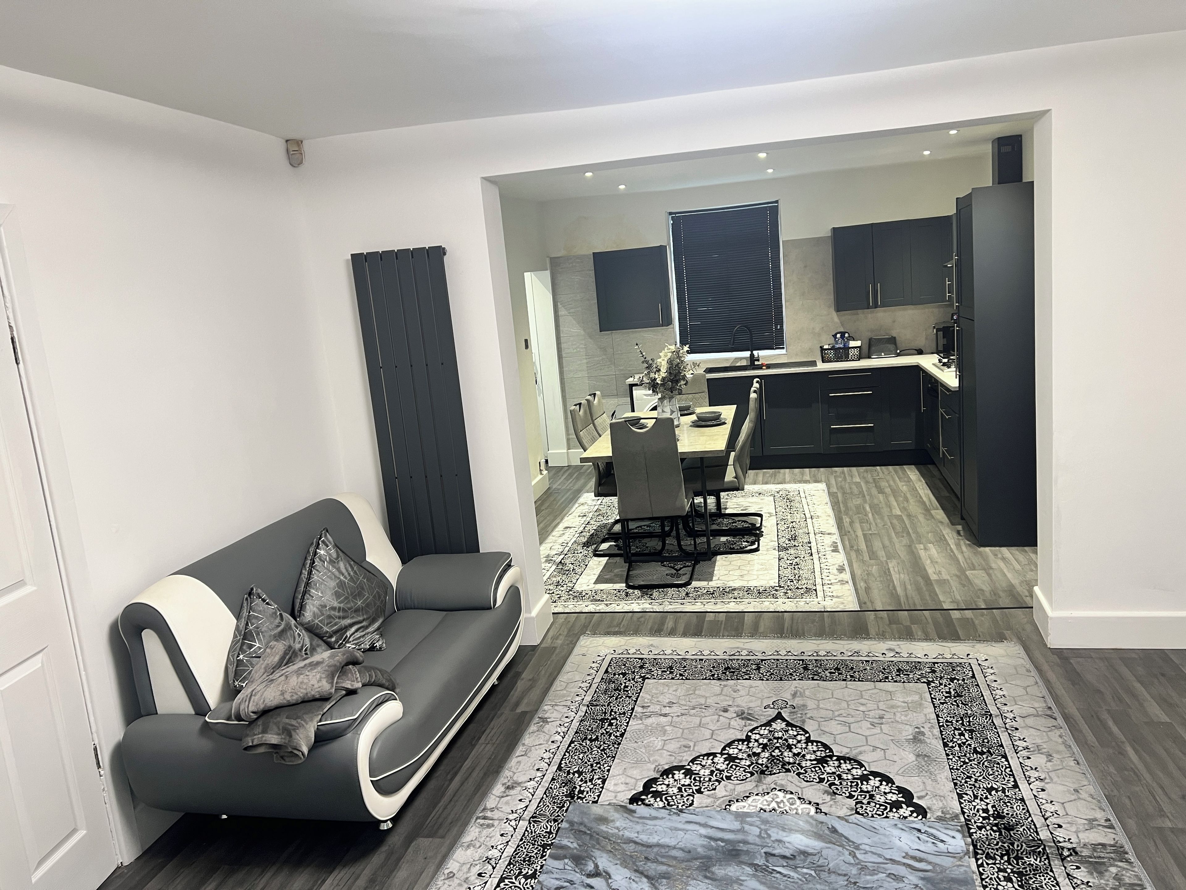 Ein modernes Wohnzimmer mit einer Couch, einem Essbereich mit Tisch und Stühlen sowie einer Küche mit dunklen Schränken.
