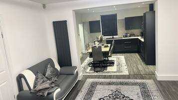Ein modernes Wohnzimmer mit einer Couch, einem Essbereich mit Tisch und Stühlen sowie einer Küche mit dunklen Schränken.