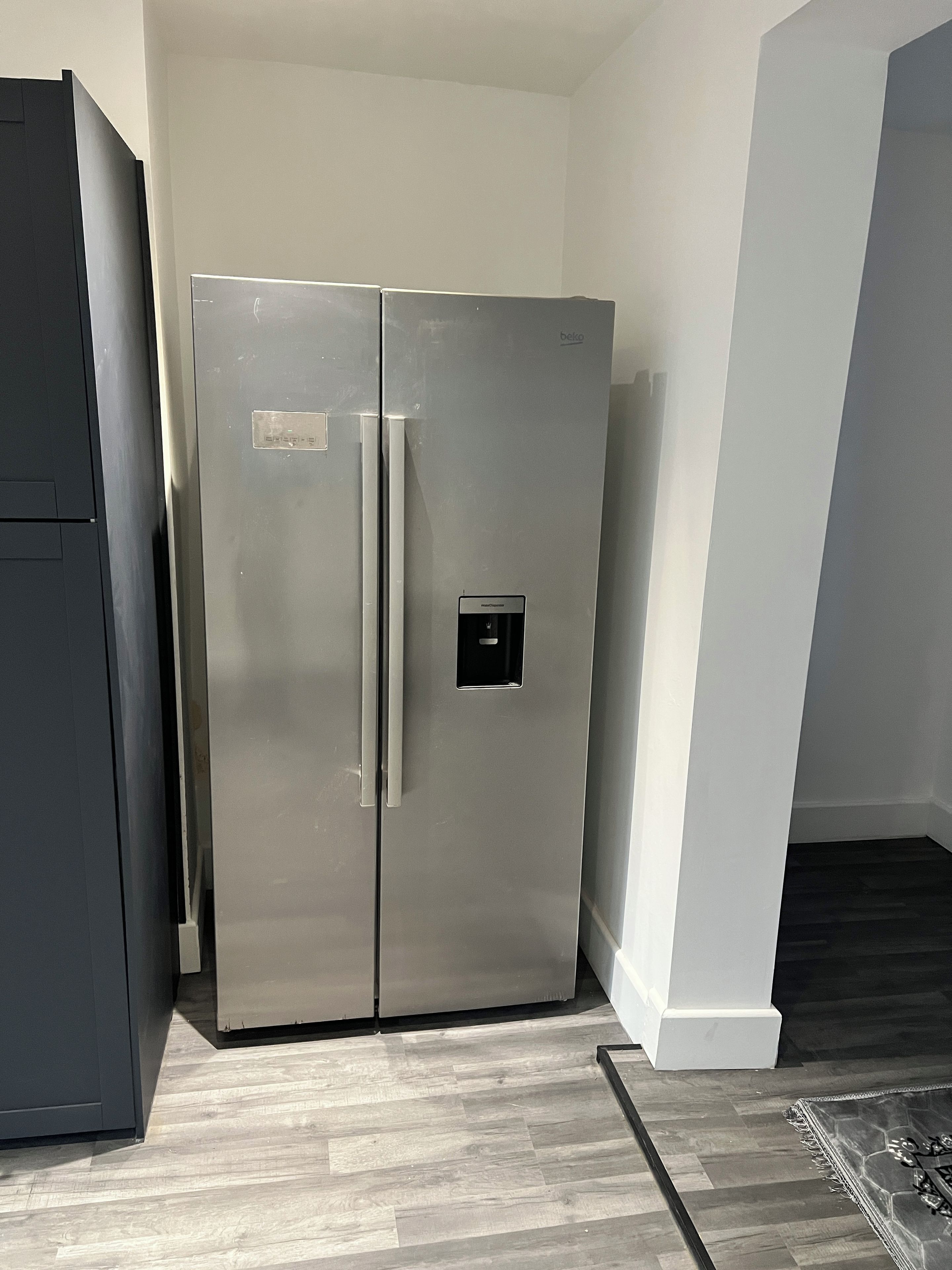 Ein Edelstahl-Kühlschrank in einer Küche mit Holzboden und einem dunklen Schrankschrank.