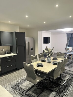 Una cocina moderna con armarios oscuros, un refrigerador empotrado y una zona de comedor con una mesa preparada para cuatro.
